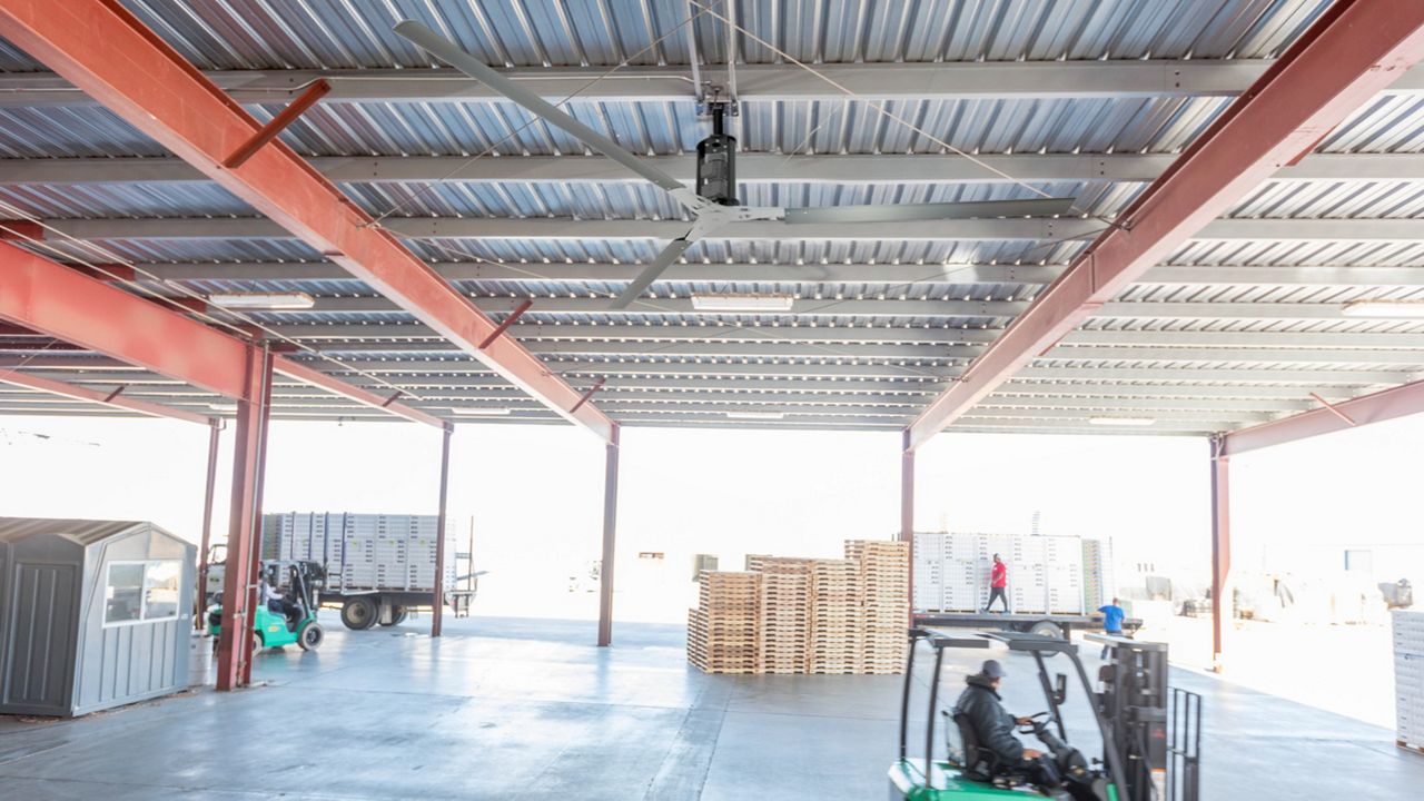 A black ceiling fan with three blades hanging in an automobile repair shop above a semi-truck