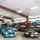 A black ceiling fan with three blades hanging in a car shop above multiple vintage cars