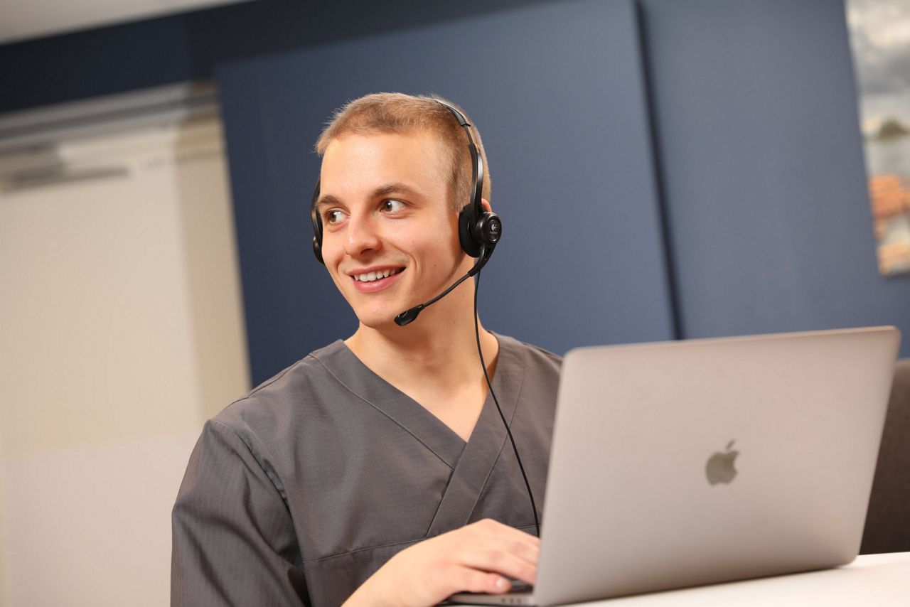 Työntekijä hymyilee headset päässä tietokoneella
