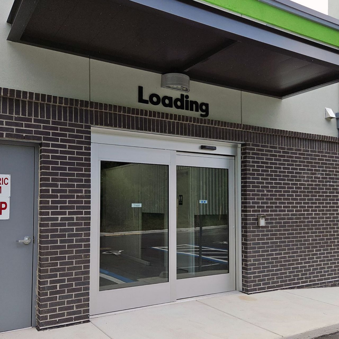 A clear, single-slide automatic door on a brick building with the word "loading" over the door.