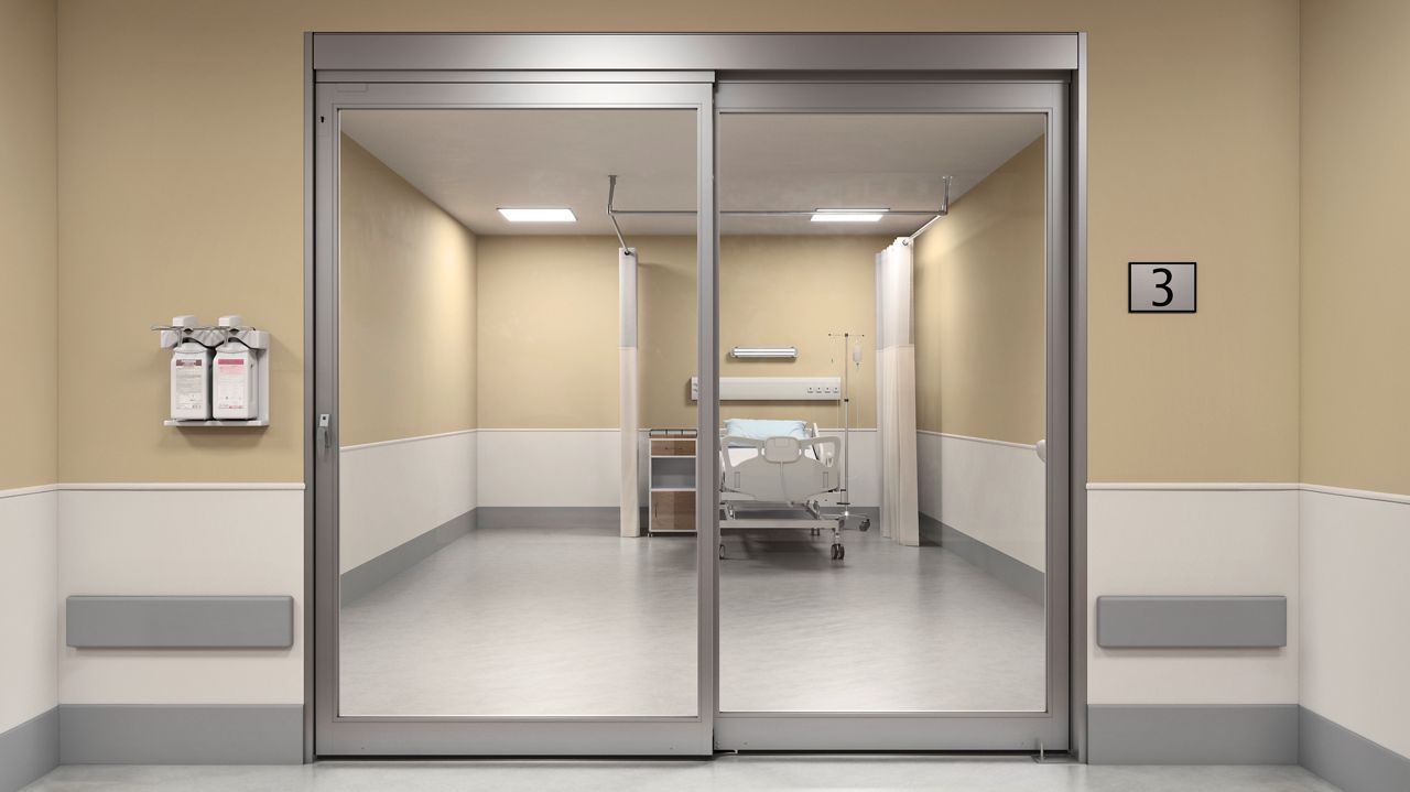 ICU sliding glass door providing clear visibility into a hospital patient room with bed, curtain, and medical equipment.