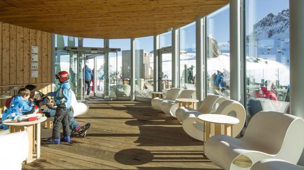 Entrada de hotel con interior de madera, paredes de cristal y puertas automáticas en un entorno alpino.