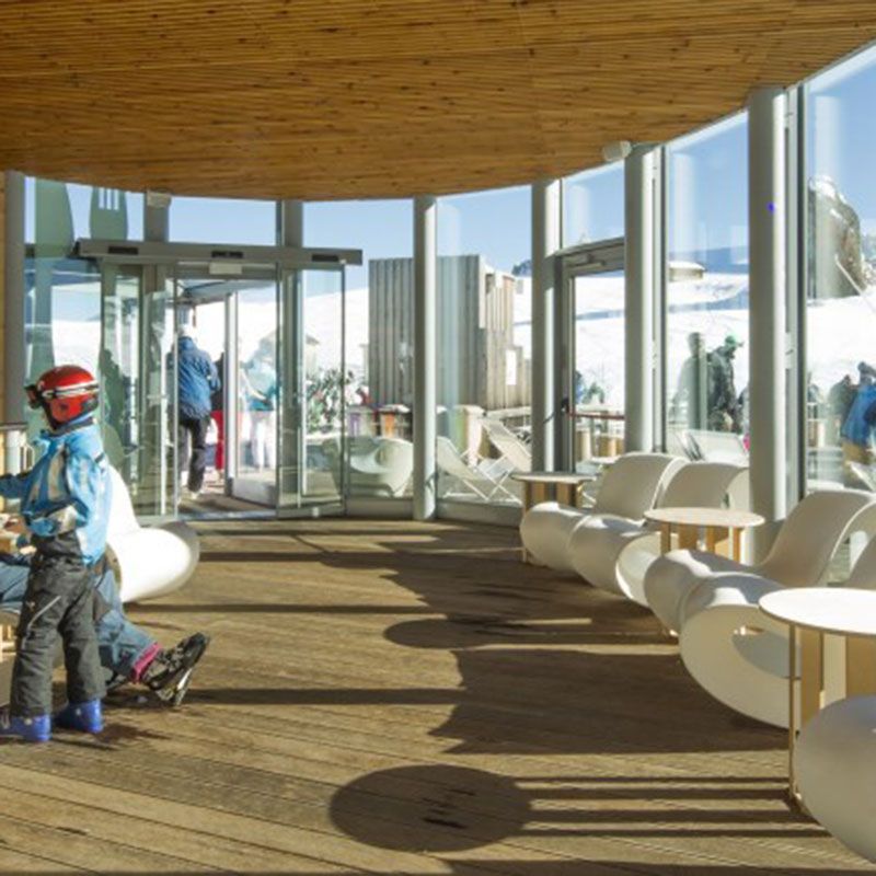 Vhod v hotel z leseno notranjostjo, stekleno steno in avtomatskimi vrati v alpskem okolju.