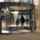 Two persons walking through revolving doors. The door has arrows on it and on the side of the doors there are pillars and trashcans. 