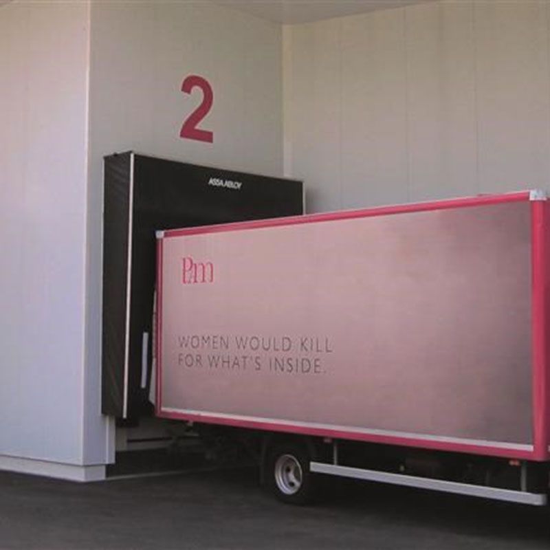 En lastbil med pink detaljer og PAM-logoet bakket op til en læsserampe.