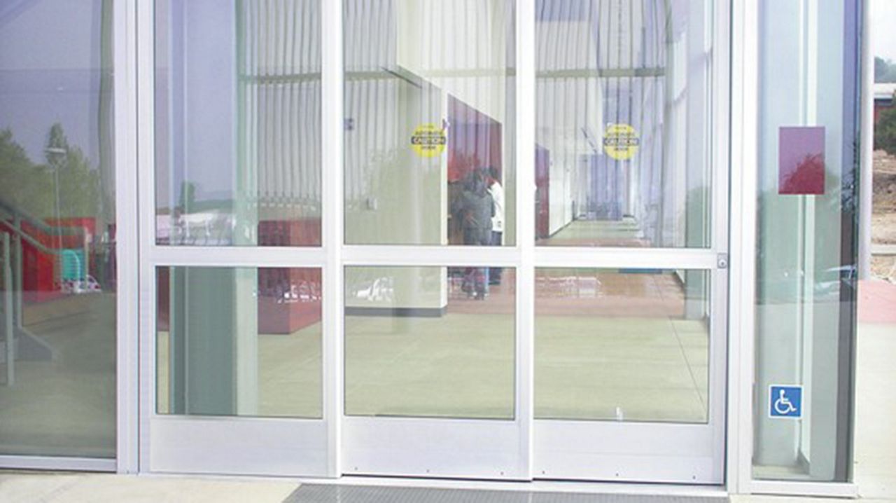 Vista frontal de las puertas ASSA ABLOY SL500 Telescopic en un edificio público con paredes de cristal.