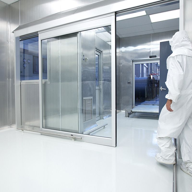 Hospital staff dressed in protection clothes and mask walking towards an open clean room door in a hospital.