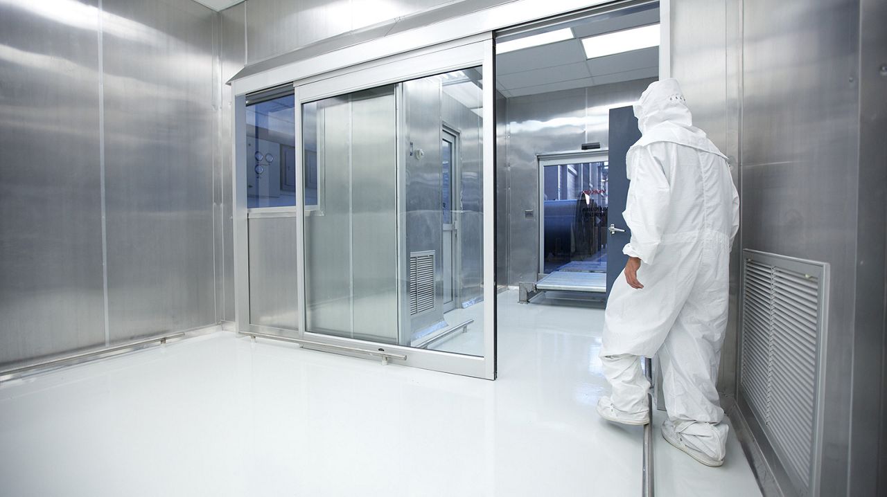Hospital staff dressed in protection clothes and mask walking towards an open clean room door in a hospital.