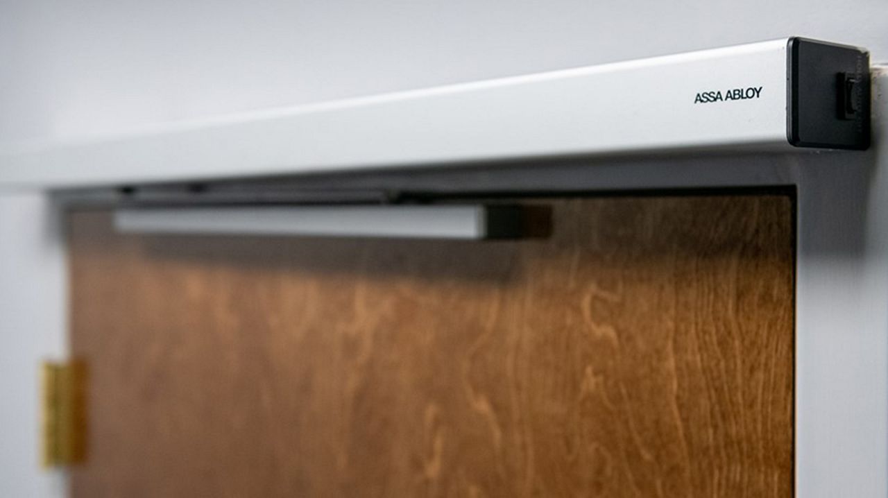 Gros plan de l’opérateur de porte battante ASSA ABLOY SW60 sur une porte en bois marron.