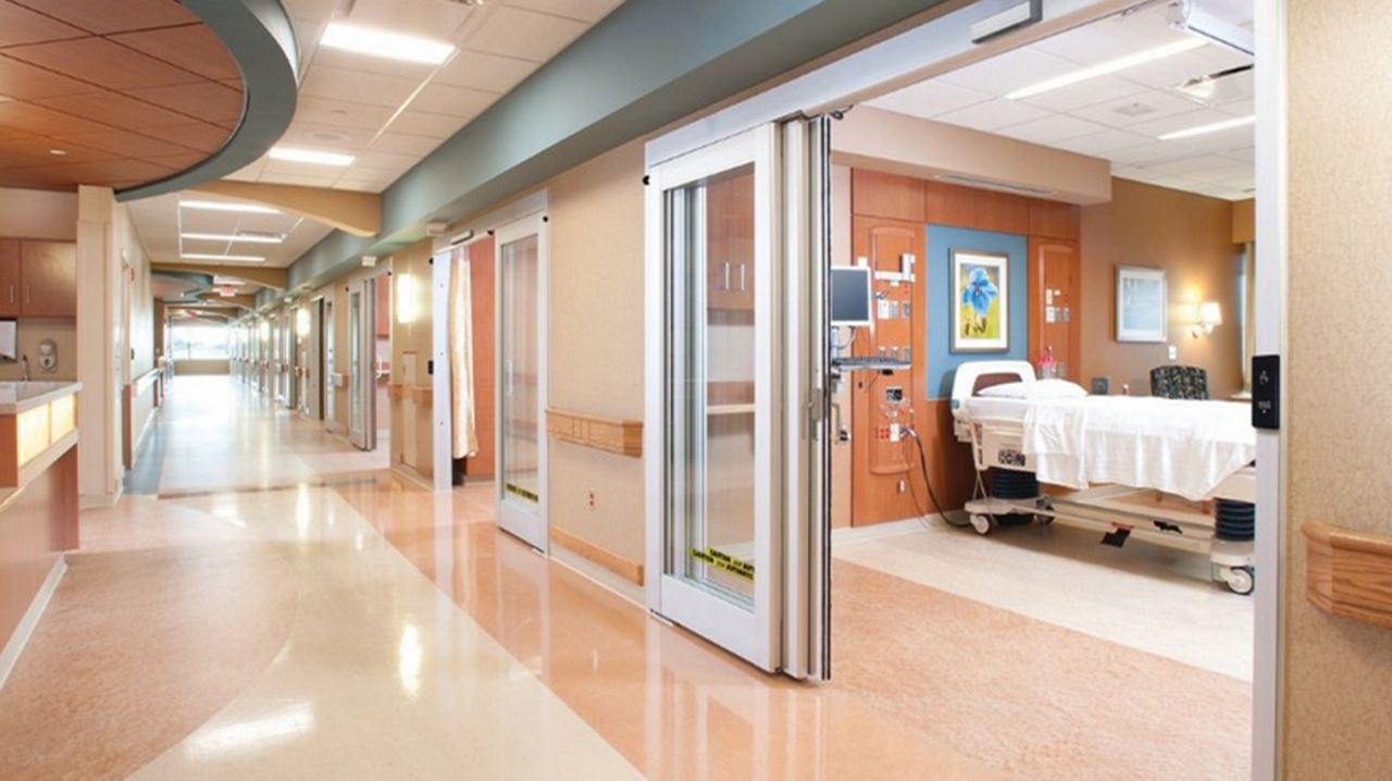 A glass touchless door in a hospital where you can see a hospital bed inside. 