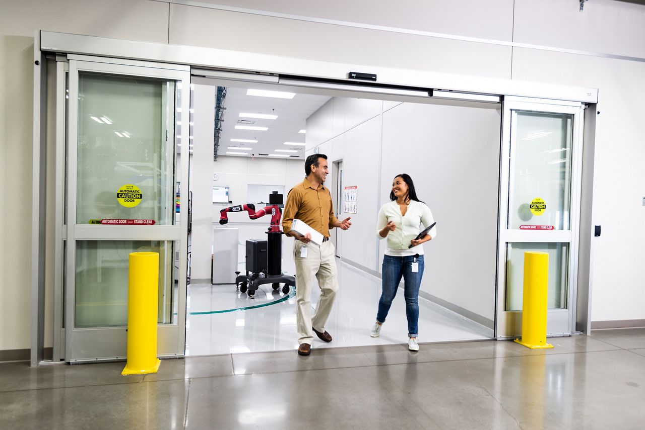 2 personnes marchent en parlant à travers des portes coulissantes automatiques ouvertes dans un environnement de recherche.