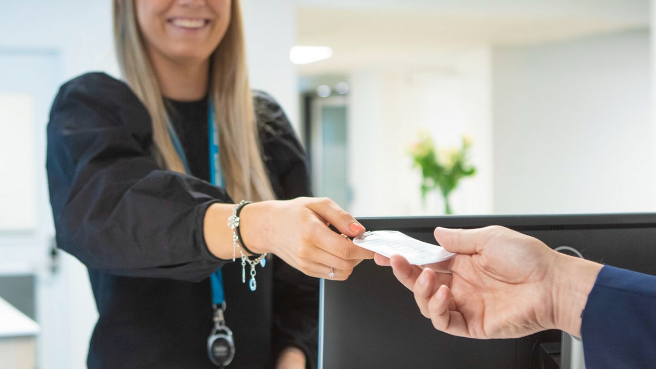 Kvinna i svart tröja ger över ett passerkort till en annan person.