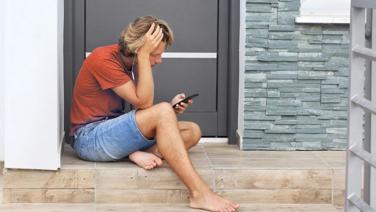 Persoon zit buiten bij een voordeur en kijkt op een mobiele telefoon