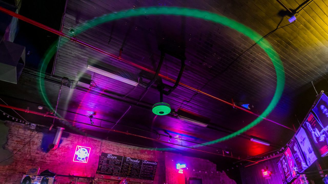 A silver fan with 5 blades and a neon center in motion at a bar