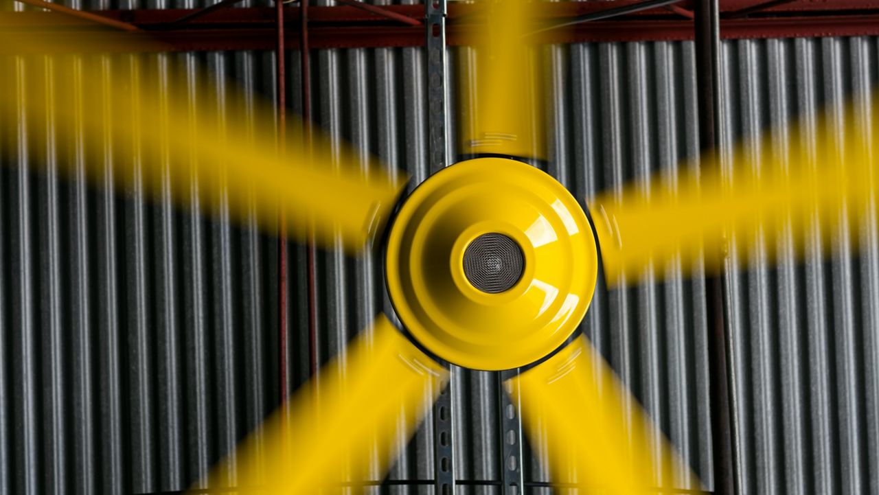 Image: A close up view of a yellow Commercial HVLS fan with the blades in motion.