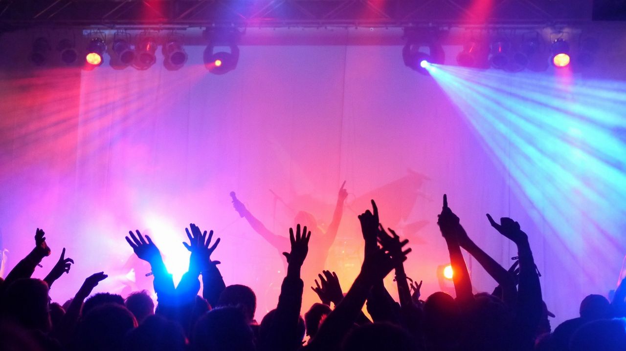 Publik på koncert sträcker upp händerna i luften mot artisten på scenen.