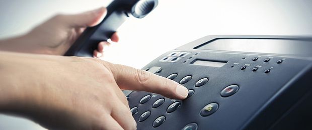 Eine Hand hält Telefonhörer, während die andere Hand eine Taste drückt
