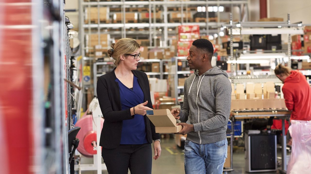 Två personer kommer gåendes i lagerlokal.