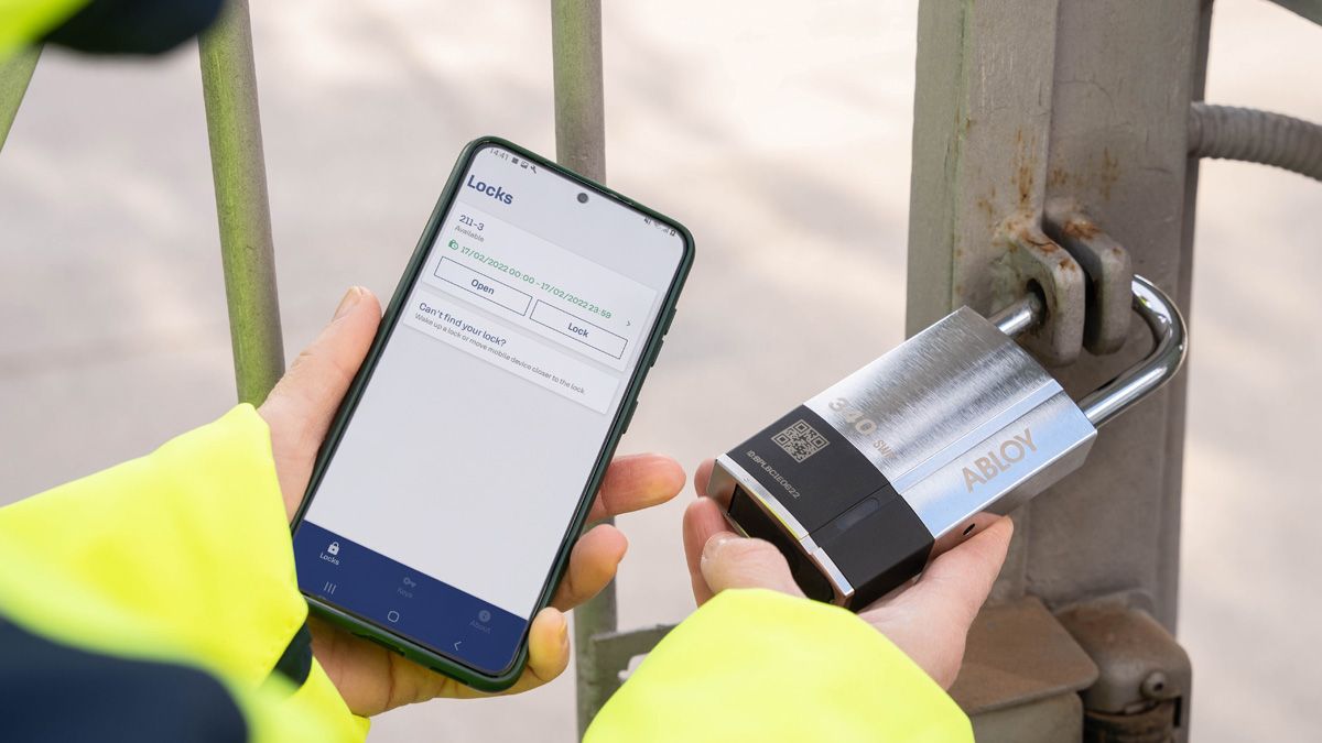 En mand holder en ABLOY PULSE låsecylinder i hånden og en mobil