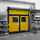 A yellow door with a grey background and shelfs. 