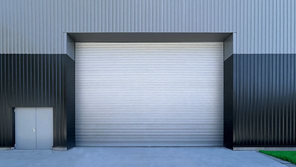 Batiment industriel gris foncé avec un rideau métallique isolé et une petite porte d'entrée à coté, vue de face.