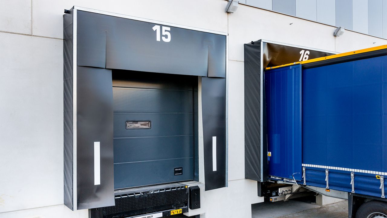 Image: Abrigo de Doca Inovadoor 202, instalado em doca de carregamento de centro logístico, com cortinas de vedação frontal em lona resistente e faixas refletivas laterais de alta visibilidade