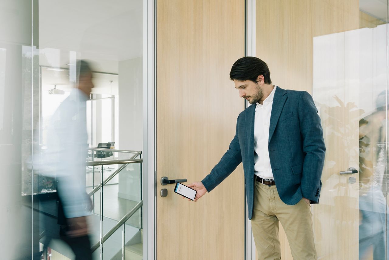 Uomo apre la porta di un ufficio con uno smartphone e una maniglia Aperio H100