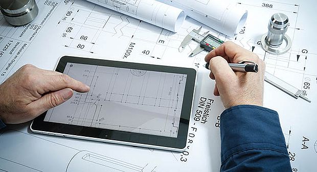 Eine Person bedient ein Tablet, welches auf einem Bauplan liegt und hält einen Stift in der Hand