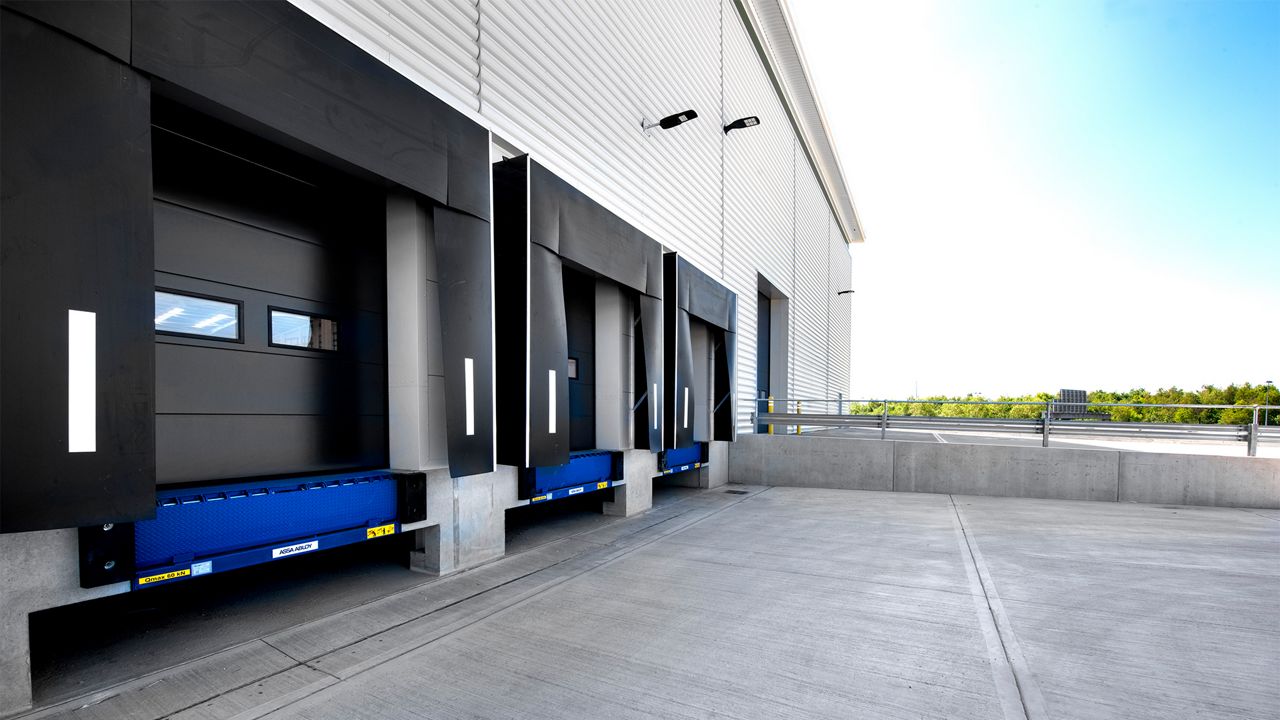 Image: Abrigo de Doca Inovadoor 202, instalado em doca de carregamento de centro logístico, com cortinas de vedação frontal em lona resistente e faixas refletivas laterais de alta visibilidade