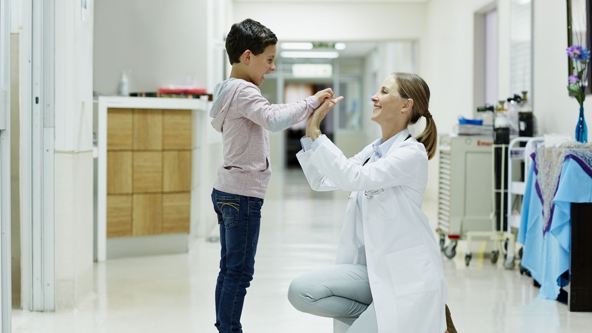 Et barn gjør high five med en kvinnelig lege i en sykehuskorridor.