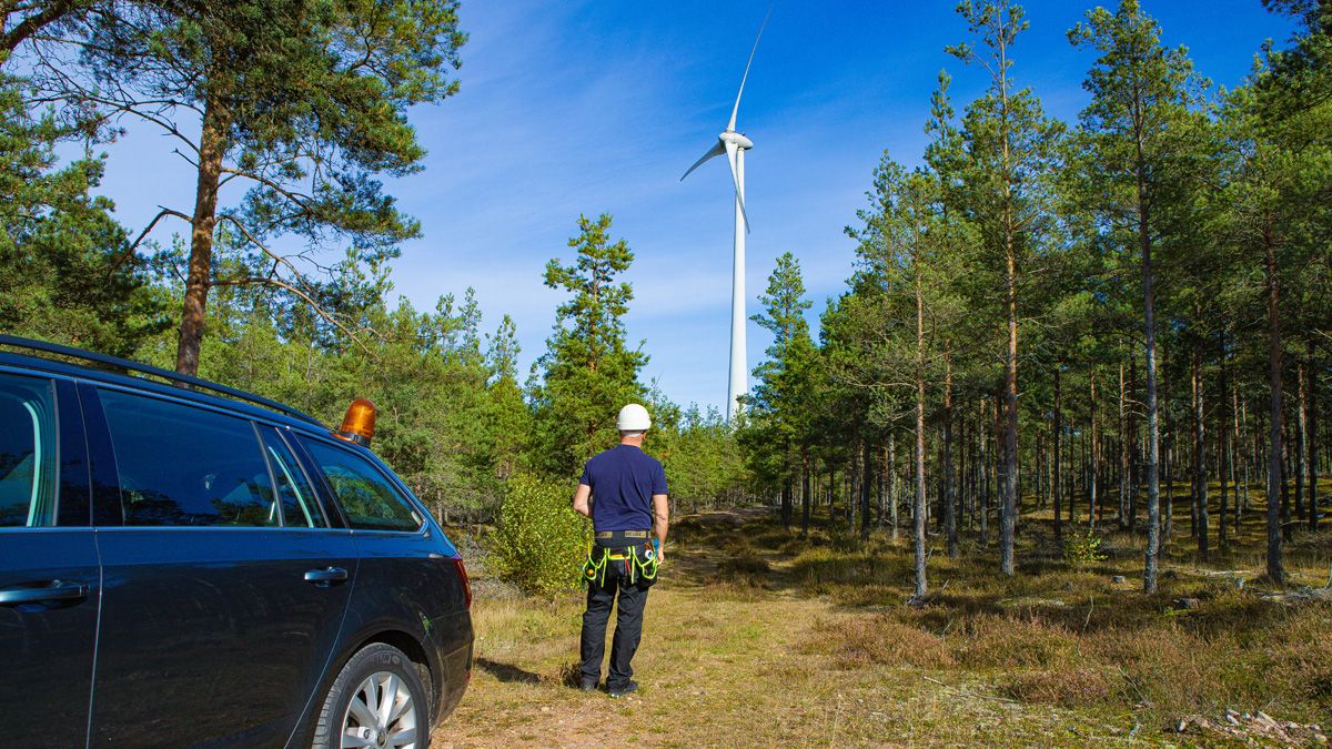 En mand står i en skov og kigger på en vindmølle