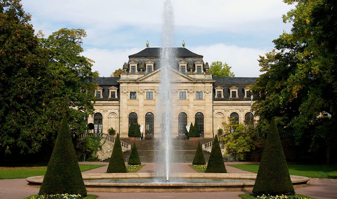 The front of a large estate with a fountain.