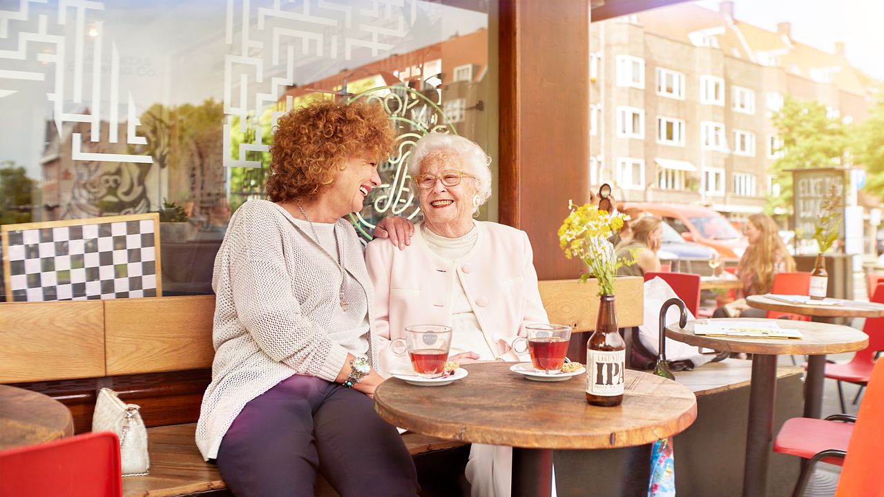 Vriendschappelijk gesprek in een café tussen een oudere vrouw en een jongere vrouw.