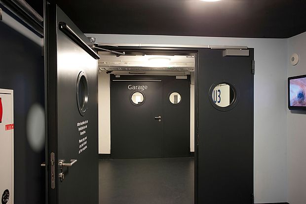 Geöffnete schwarze Tür hinter der sich eine weitere Tür mit der Beschriftung "Garage" befindet