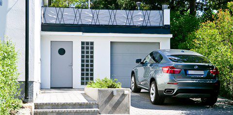 Pohled na vstupní šedé dveře a vrata před nimi stojí zaparkované auto značky BMW