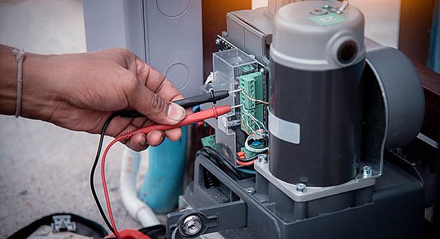 Hand steckt zwei Stecker in einen offenen Torantrieb
