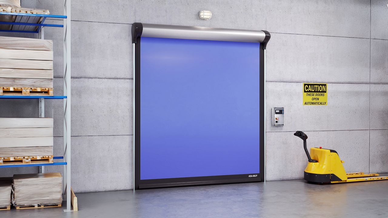Image: Porta Rápida para Indústria Alimentícia ASSA ABLOY HS9130G, azul com estrutura em aço inoxidável, instalada em área de armazenamento e logística industrial para otimizar o fluxo de materiais, manter a higiene operacional e controlar as condições