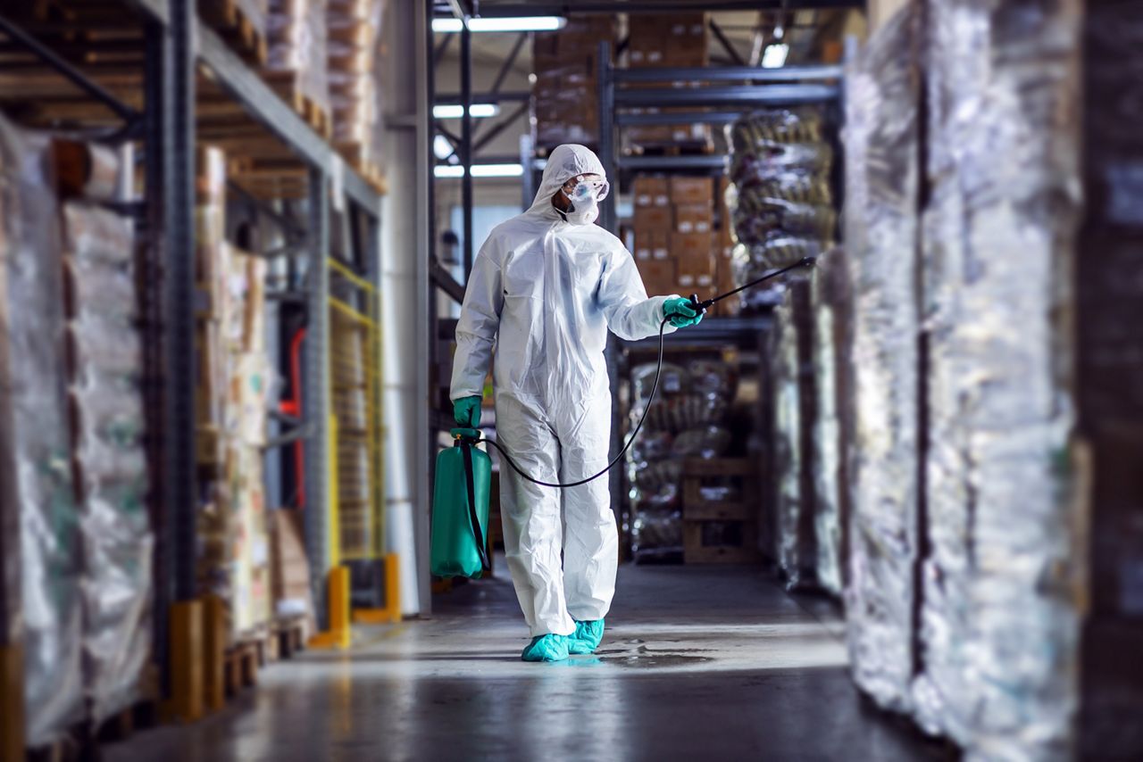 A man in a hazmat suit sanitizing a warehouse