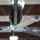 A fan with 5 black blades and a silver center hanging in a warehouse over multiple vintage cars
