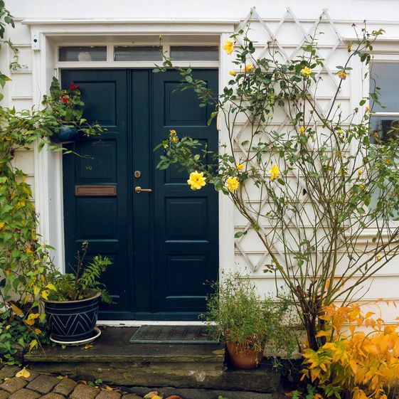 Svart dør på hvitt hus omgitt av blomster.