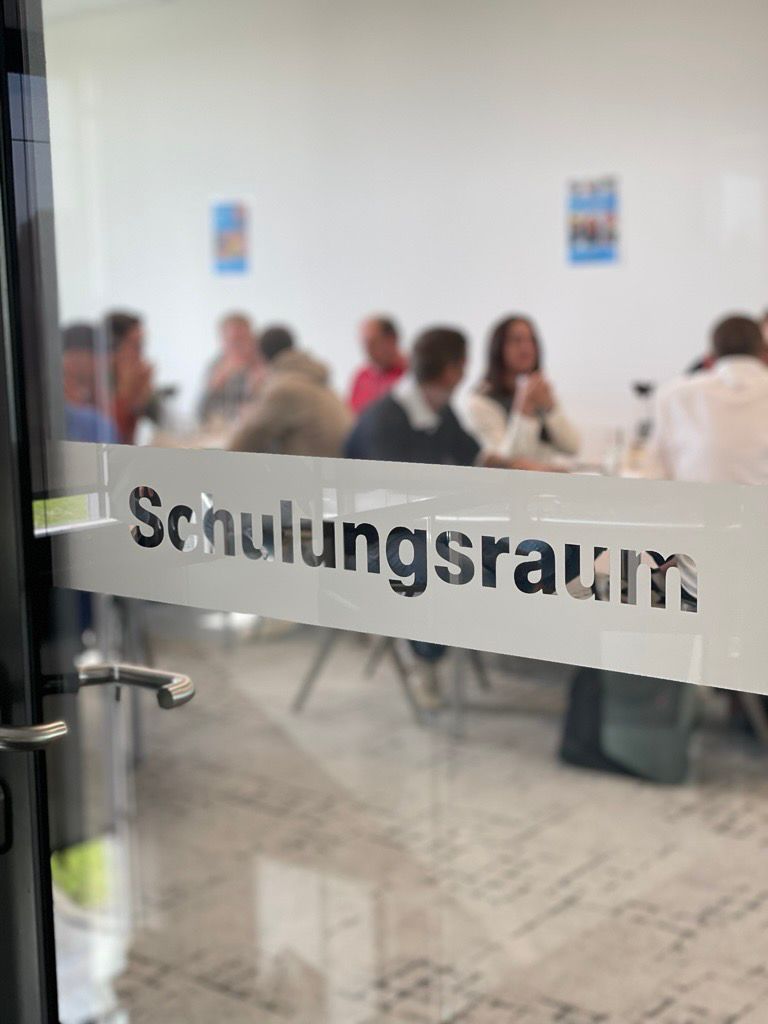 Glastür mit Aufschrift Schulungsraum hinter der Personen sitzen