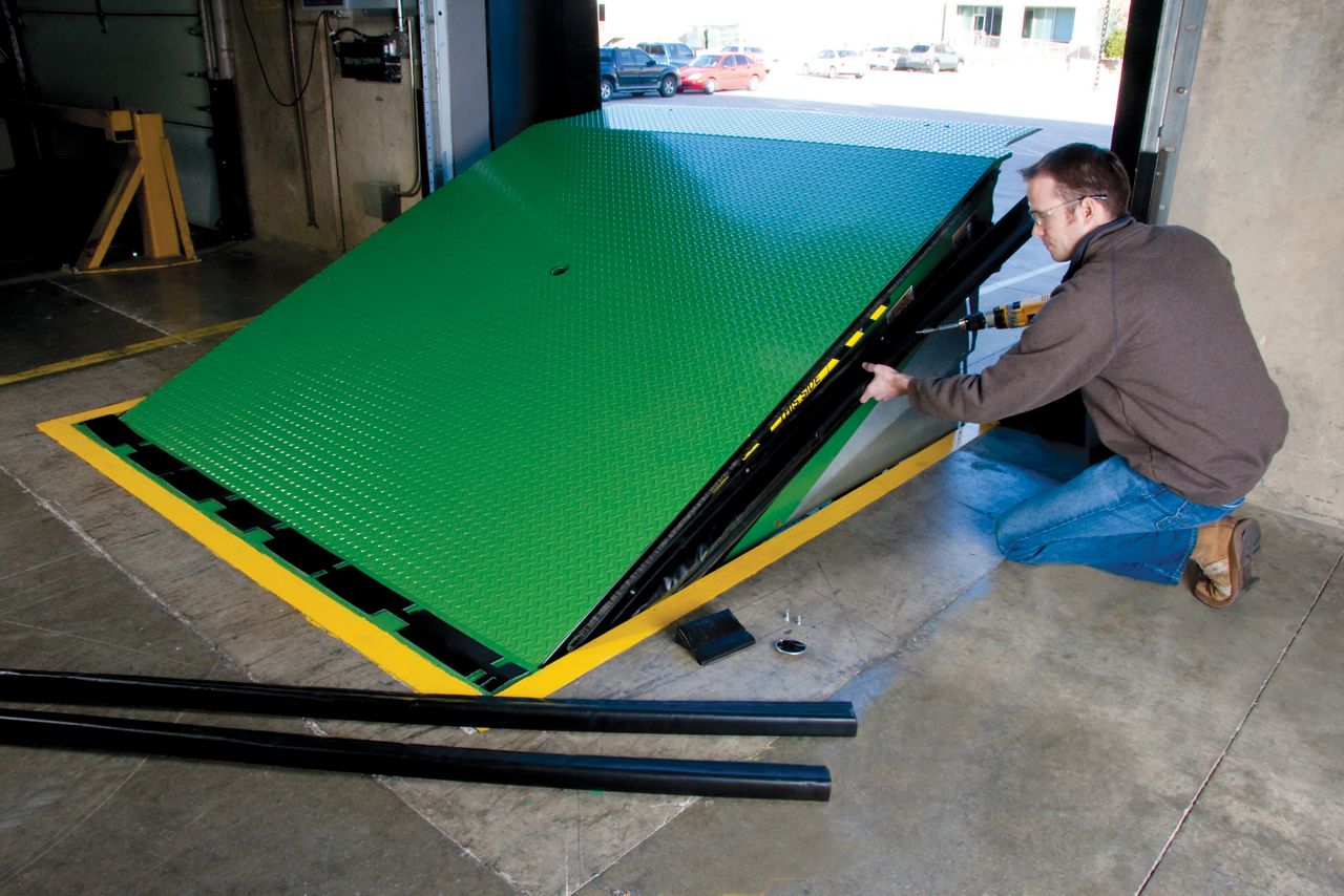 A man pulling up a green dock leveler at a warehouse