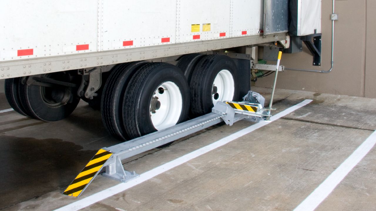 A manually operated, surface-mounted device for efficient wheel anchoring with half of a trailer in view.