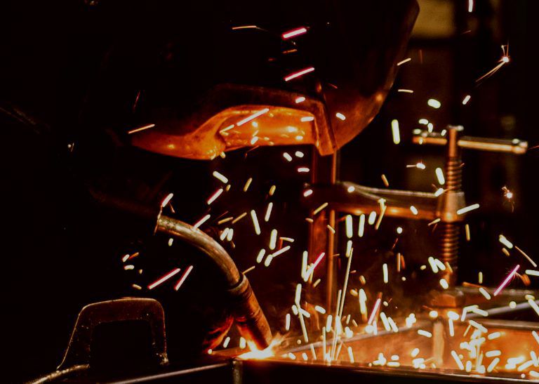 A man in a mask welding metal with sparks flying all around him