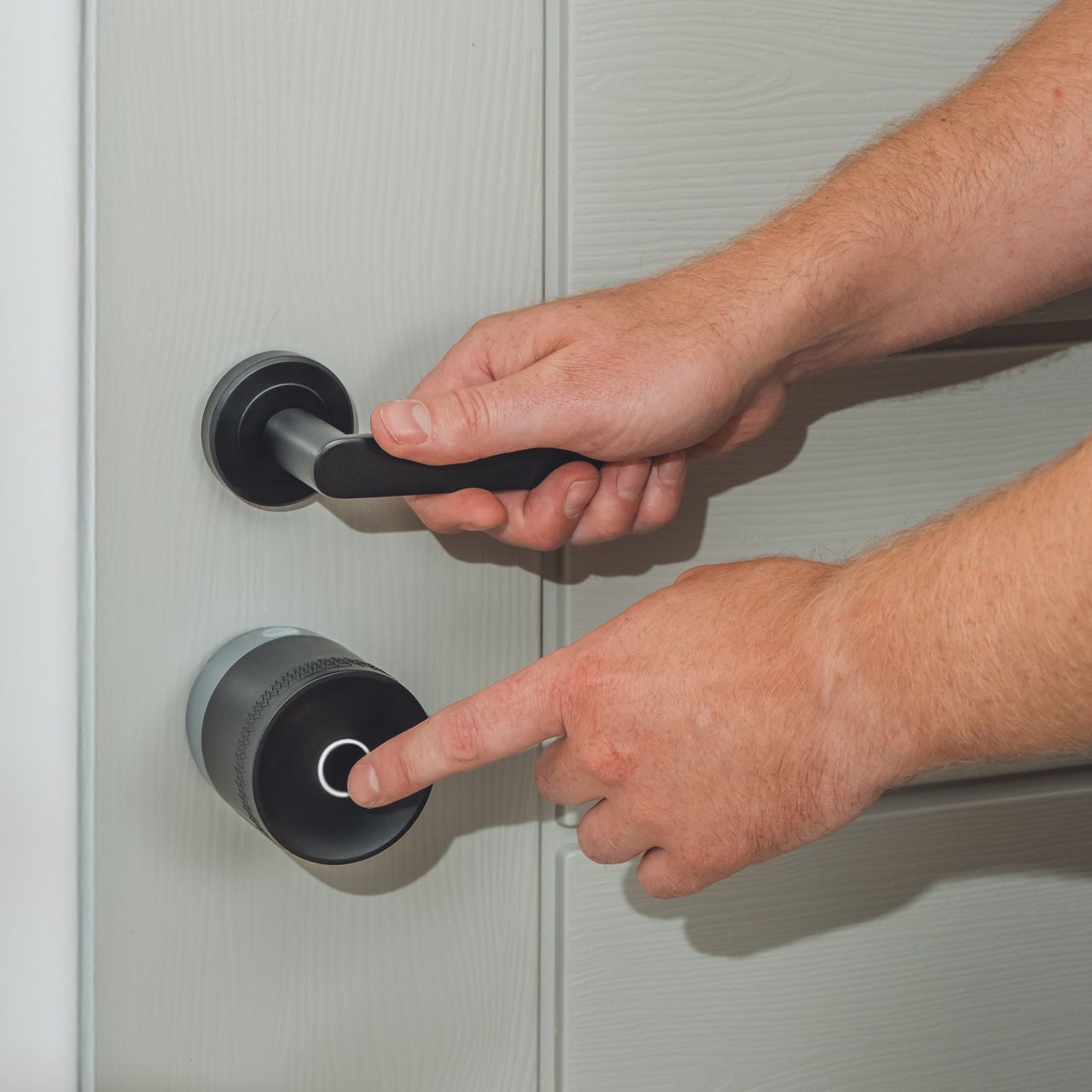 Image: Smart lock with green LED ring and black door handle on light wood door slightly open to outdoor view