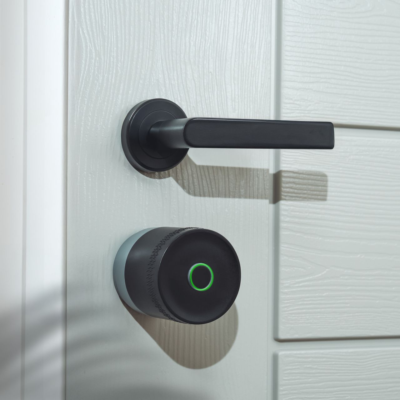 Image: Smart lock with green LED ring and curved metallic door handle on gray door
