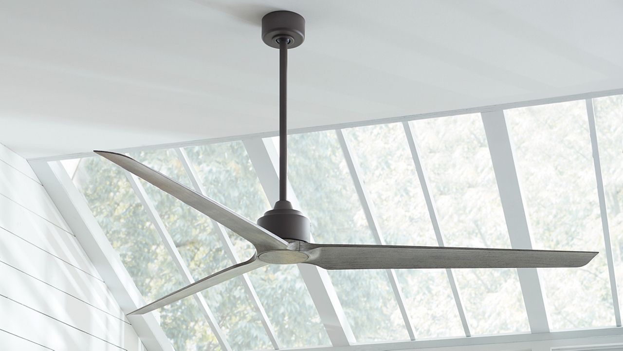 Image: A black and gray TriAire Residential Fan hanging from a white ceiling with sky lights.
