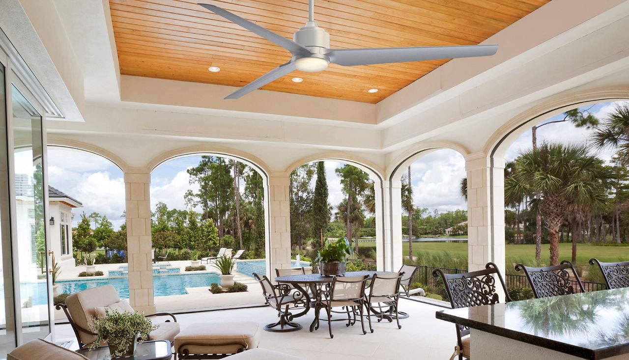 Image: A silver TriAire Residential Fan hanging outside over a covered bar by a pool. 