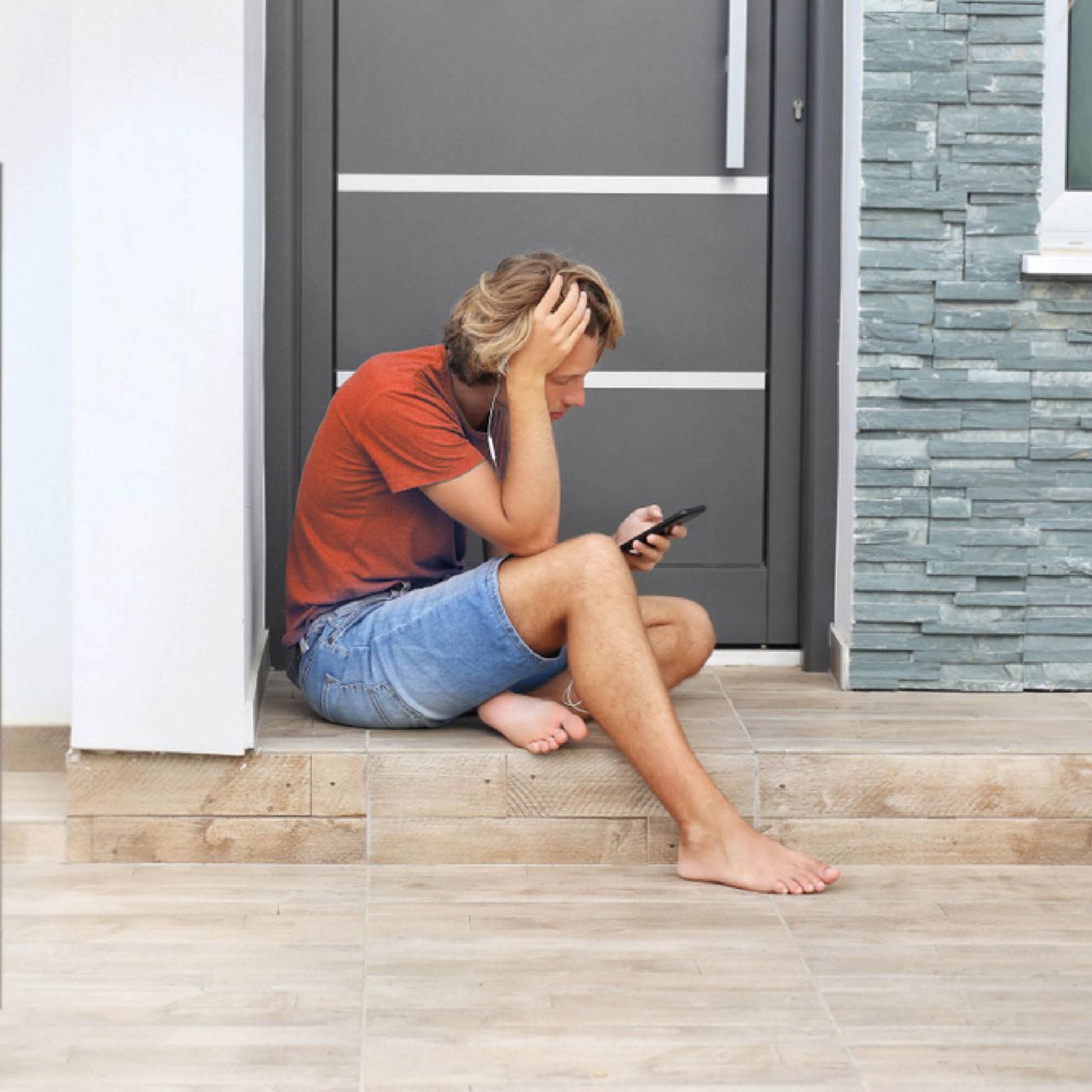Persoon zit buiten bij een voordeur en kijkt op een mobiele telefoon