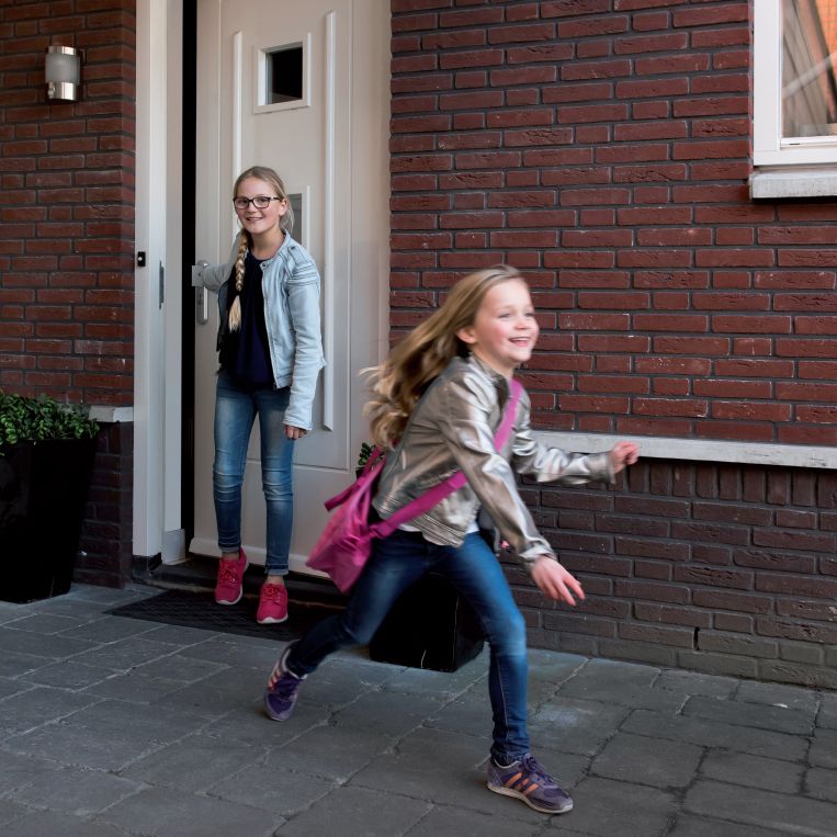 Kinderen lopen naar buiten bij een woning met open voordeur